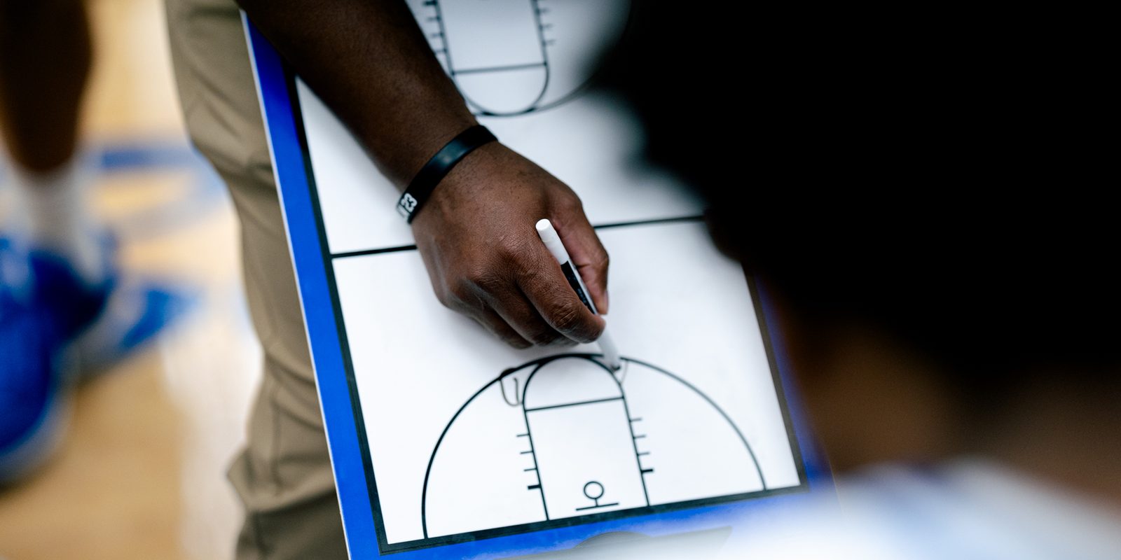 Close-up of a hand drawing a basketball play on a blue clipboard